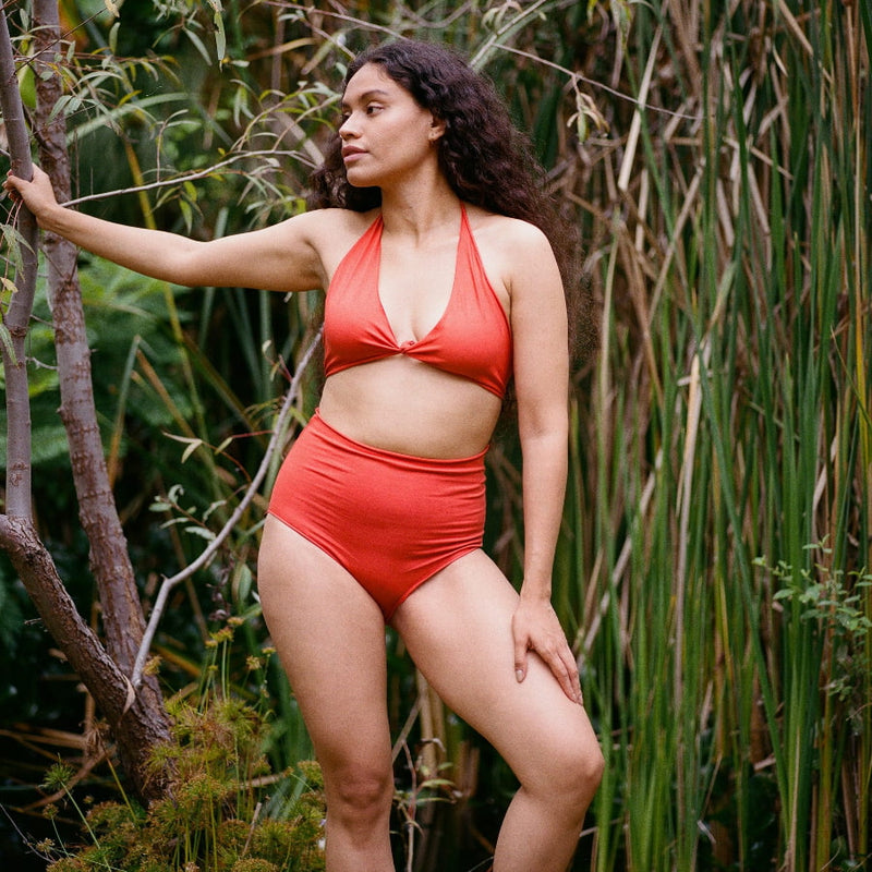 Woman in a red organic cotton bikini standing among tall grasses.