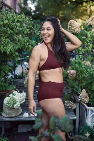 Woman in a maroon swimsuit standing outdoors with greenery around
