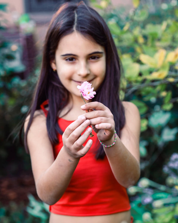 Girl outside looking at a flower wearing and orange cotton tank top.