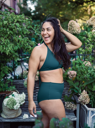Woman in green cotton bathing suit standing outdoors with plants and flowers in the background