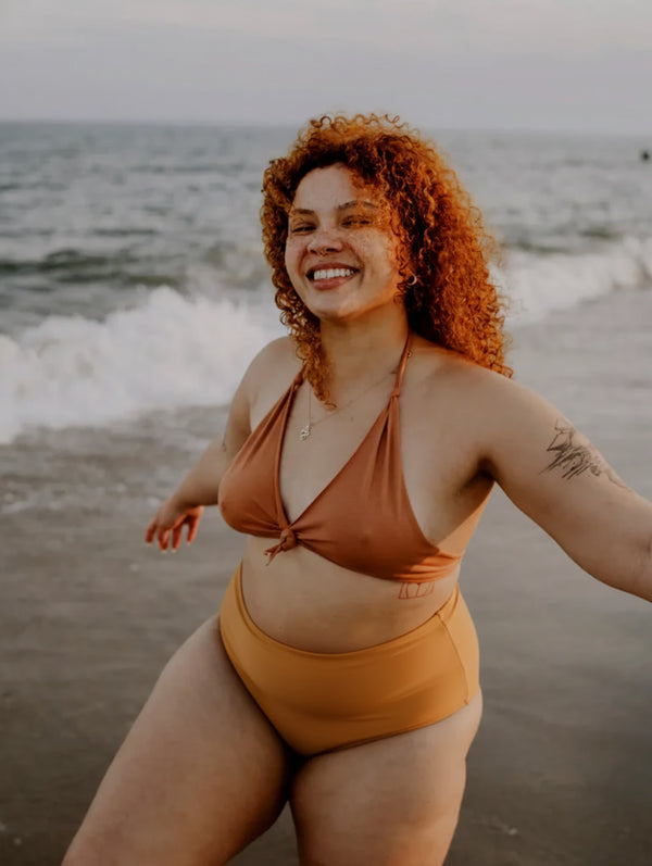 Woman in a rust-colored cotton bikini standing on a beach with ocean waves in the background